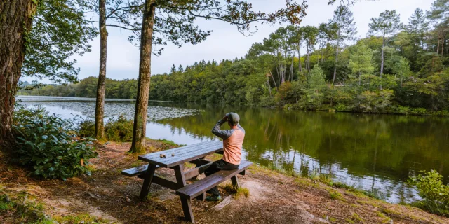 Homme assis a une table de pique-nique qui observe le paysage au bord de l'etang de Baron.