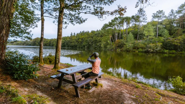 Homme assis a une table de pique-nique qui observe le paysage au bord de l'etang de Baron.