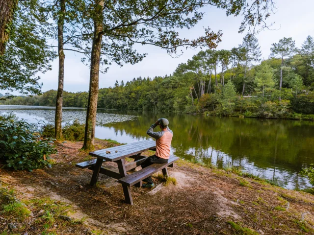 Homme assis a une table de pique-nique qui observe le paysage au bord de l'etang de Baron.